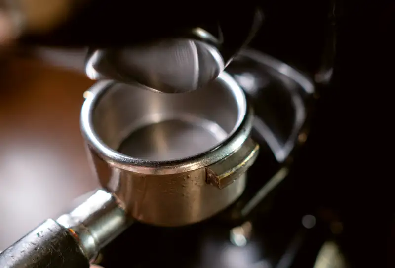 A portafilter dosed and levelled, held up against the group head, the bar behind it going soft and dark.