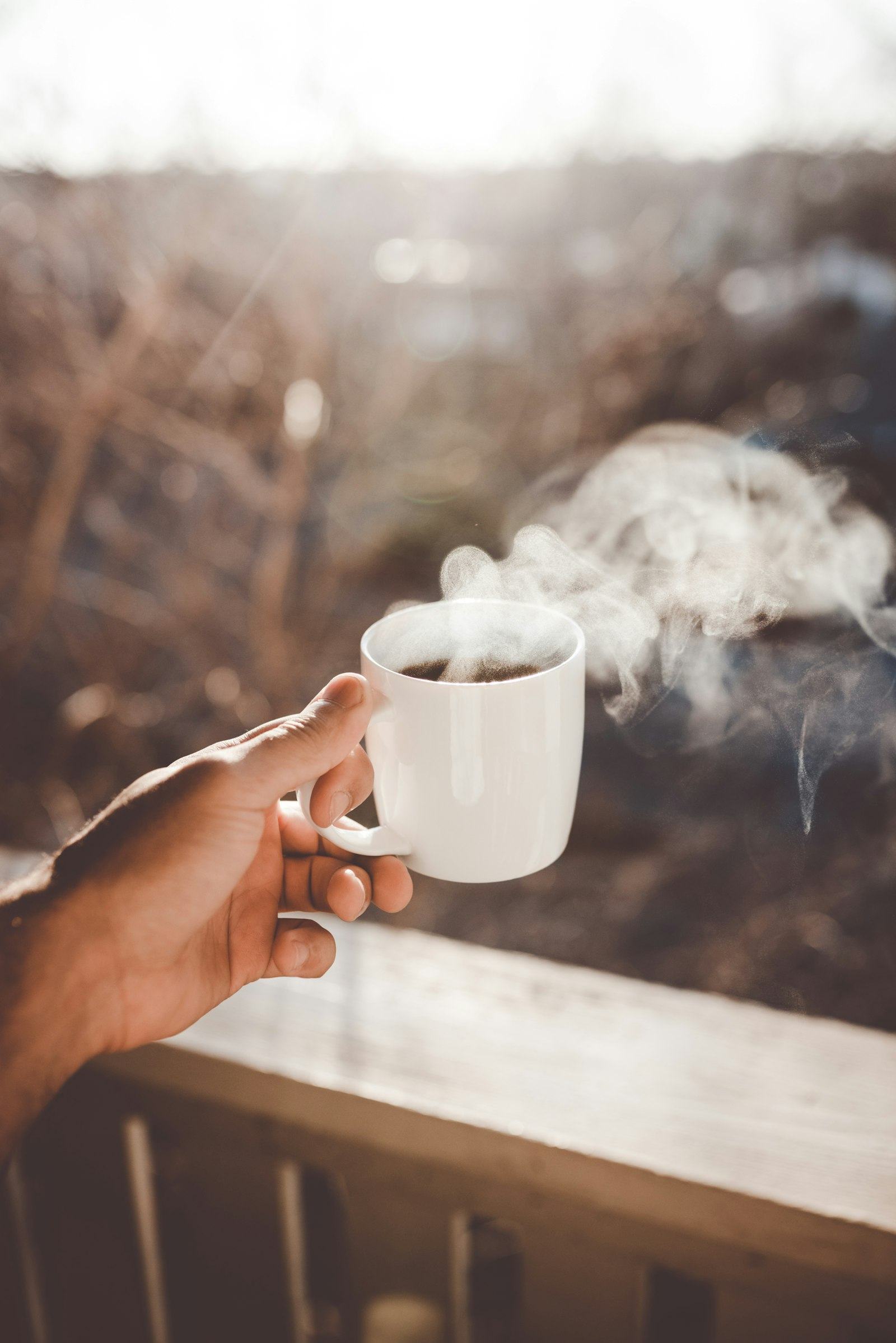 Two hands cradling a steaming cup in warm light